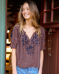 Girl standing in doorway in a gingham embroidered brown and navy top