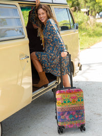 Woman with a floral dress and suitcase getting into a vintage van on a road trip.
