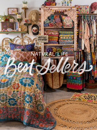 A styled bedroom and storage area filled with colorful bohemian textiles, patterned quilts, folded fabrics, woven rugs, and clothing racks. Large overlaid text reads 'NATURAL LIFE Best Sellers'.