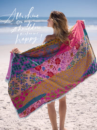 Woman holding a colorful floral beach towel on a sandy beach with ocean view
