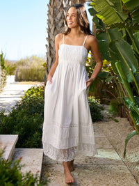 Woman in a white dress standing in a garden with greenery and a pathway.