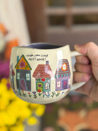 Mug with house designs and text held by a hand, blurred background